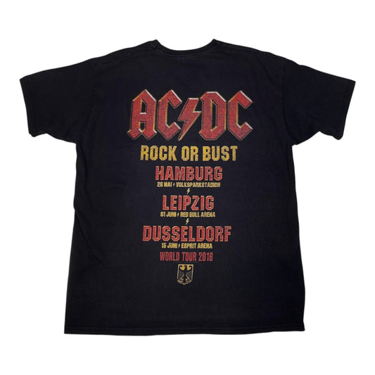 A black short-sleeve t-shirt featuring a large AC/DC 'Rock or Bust' world tour 2016 graphic on the front. The graphic displays the band's name in their signature red and yellow font, followed by the tour cities (Hamburg, Leipzig, Dusseldorf) and dates in red and yellow text, with a small black eagle crest at the bottom.