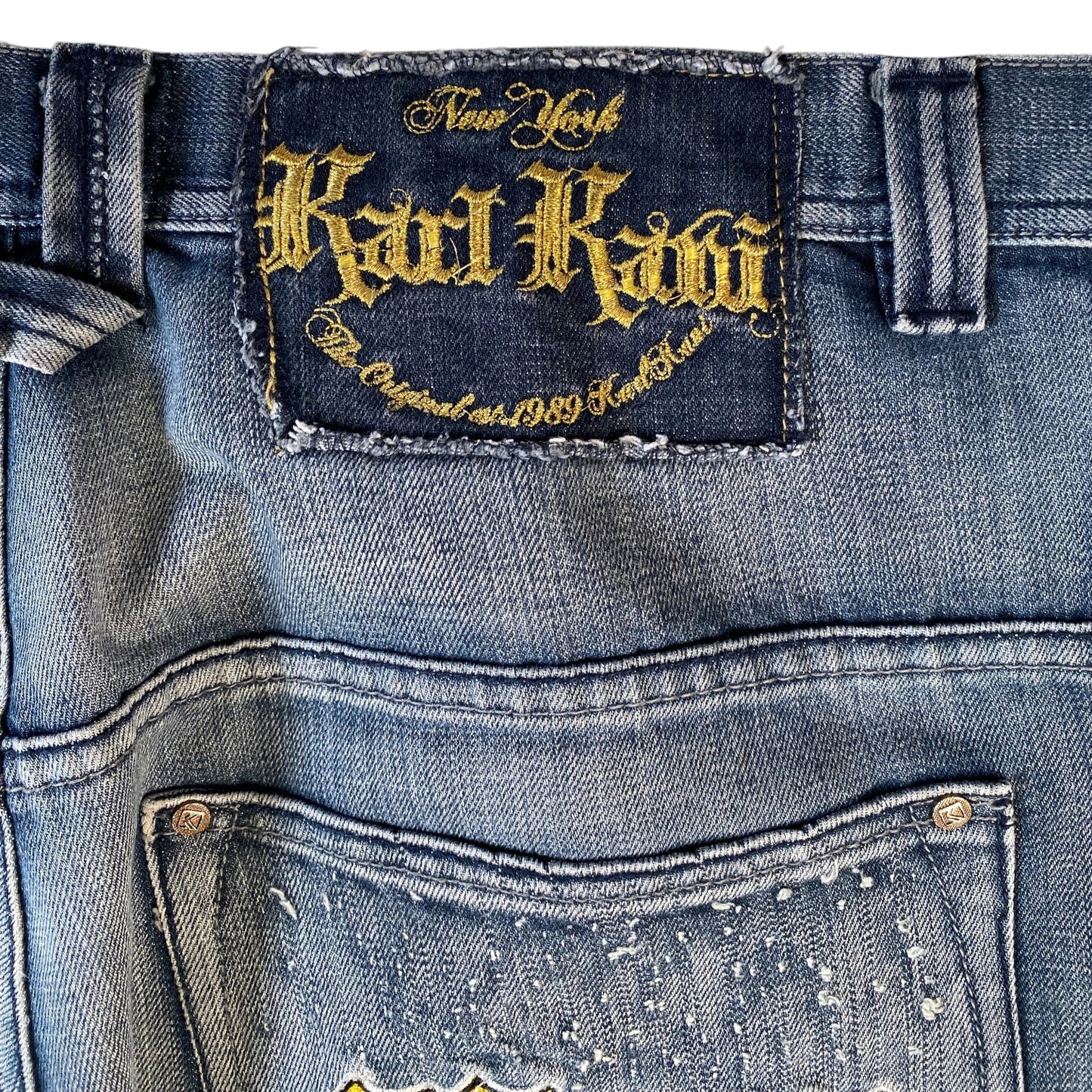 Close-up of the back waistband and pocket area of light-wash blue denim jeans, showing a dark blue patch with gold embroidered 'New York Karl Lagerfeld' branding and distressed details.
