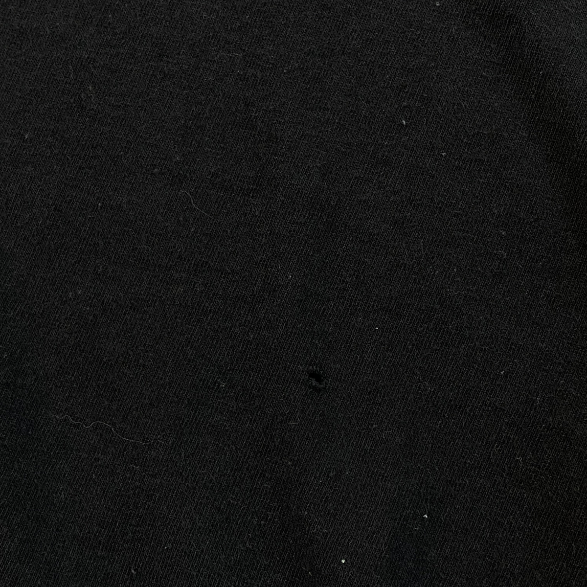 Digg It Thrift & Vintage black cotton t-shirt fabric showing a small hole defect in the material