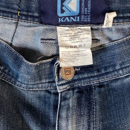 Close-up of blue denim jeans showing the inner waistband, Kani brand label, care instructions tag, and a brass button.