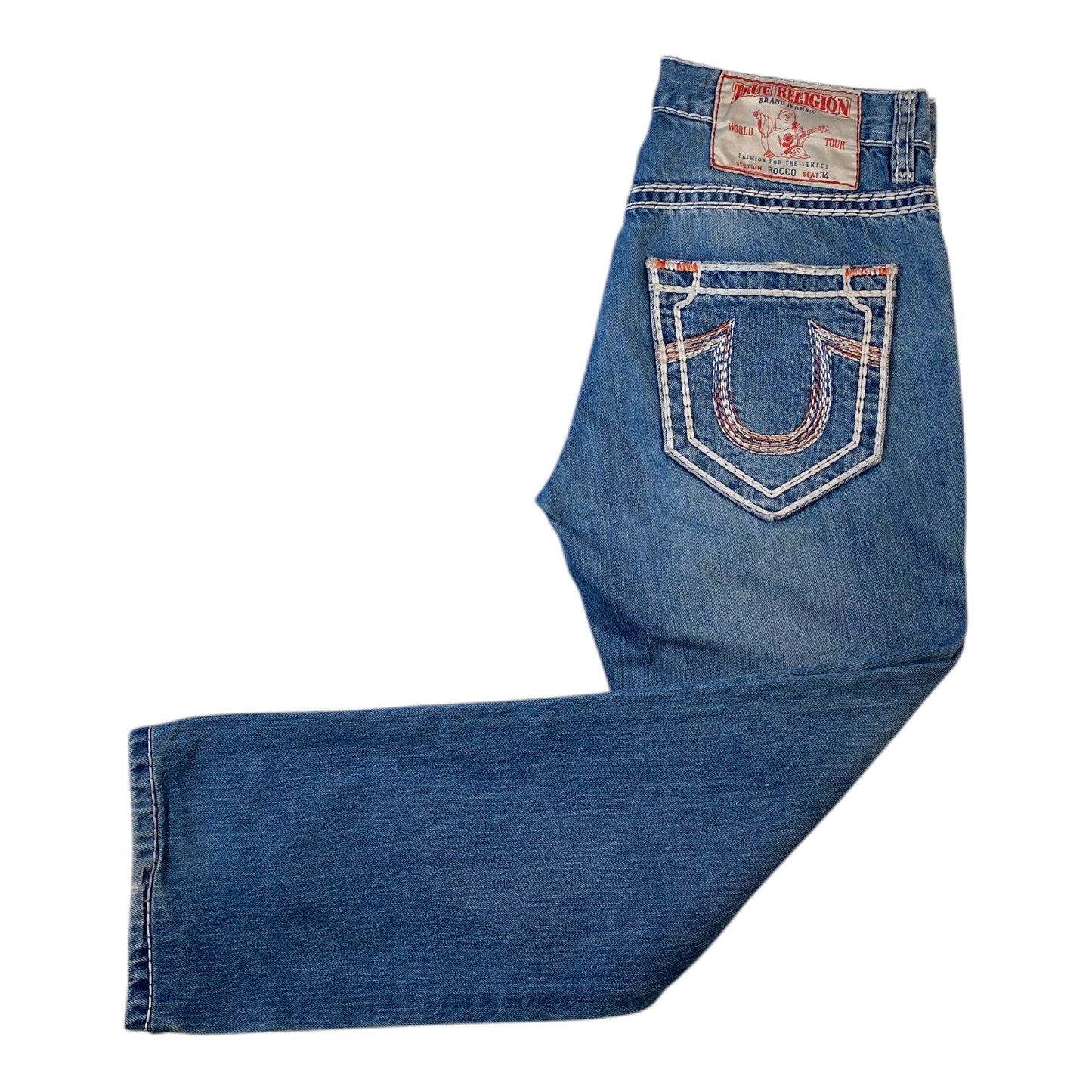 A pair of blue denim jeans laid flat on a white background, showing the back pocket with decorative contrast stitching and a visible True Religion brand patch.