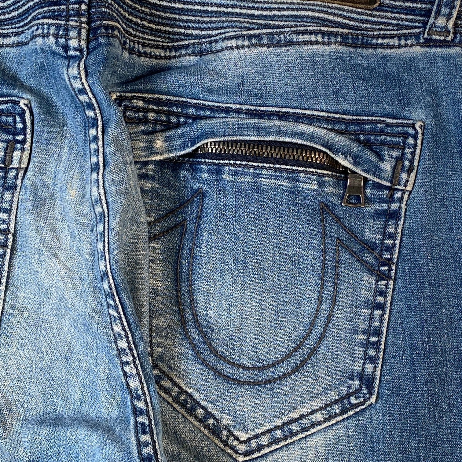 Close-up of the back pocket of blue denim jeans, showing a zippered pocket opening and contrast stitching.