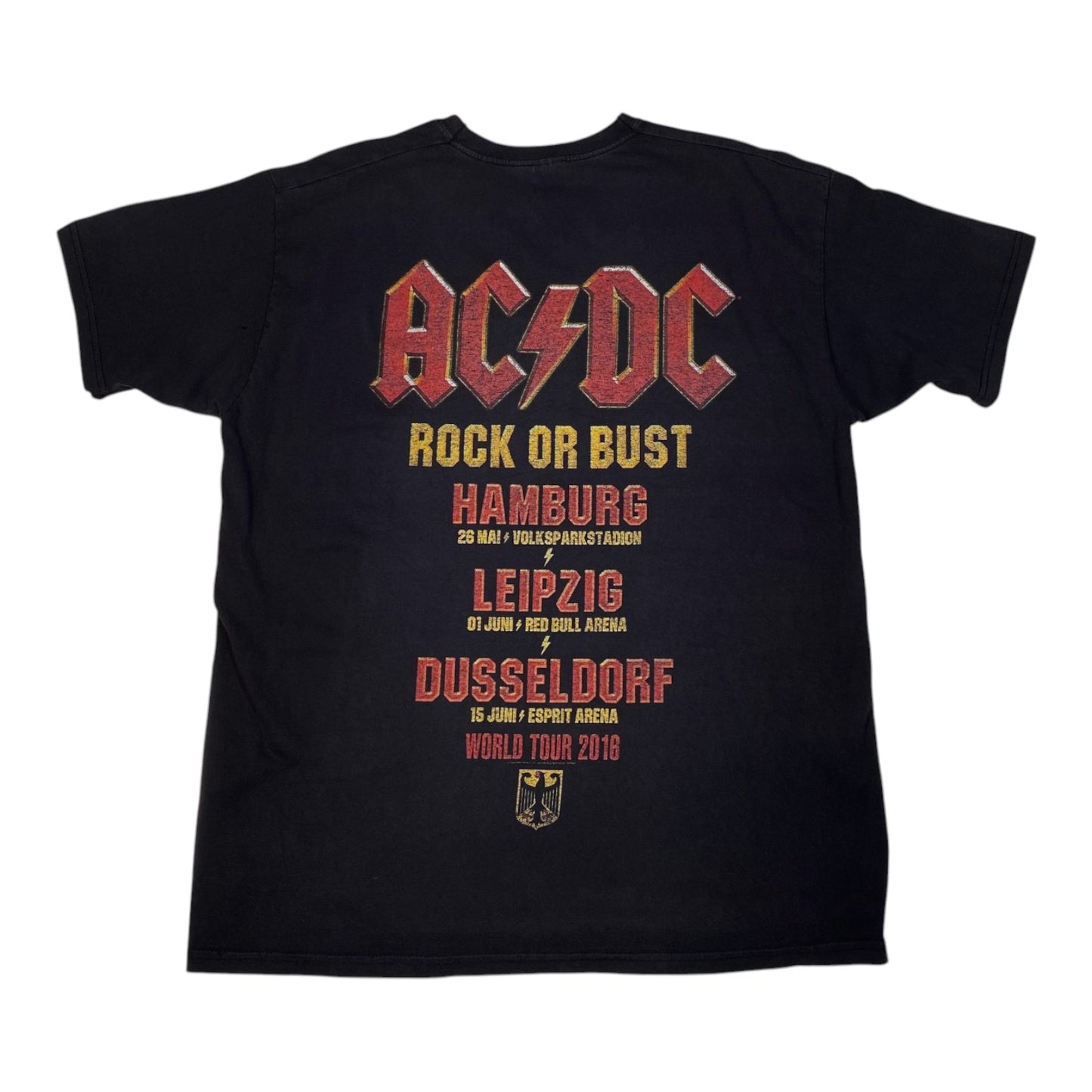 A black short-sleeve t-shirt featuring a large AC/DC 'Rock or Bust' world tour 2016 graphic on the front. The graphic displays the band's name in their signature red and yellow font, followed by the tour cities (Hamburg, Leipzig, Dusseldorf) and dates in red and yellow text, with a small black eagle crest at the bottom.