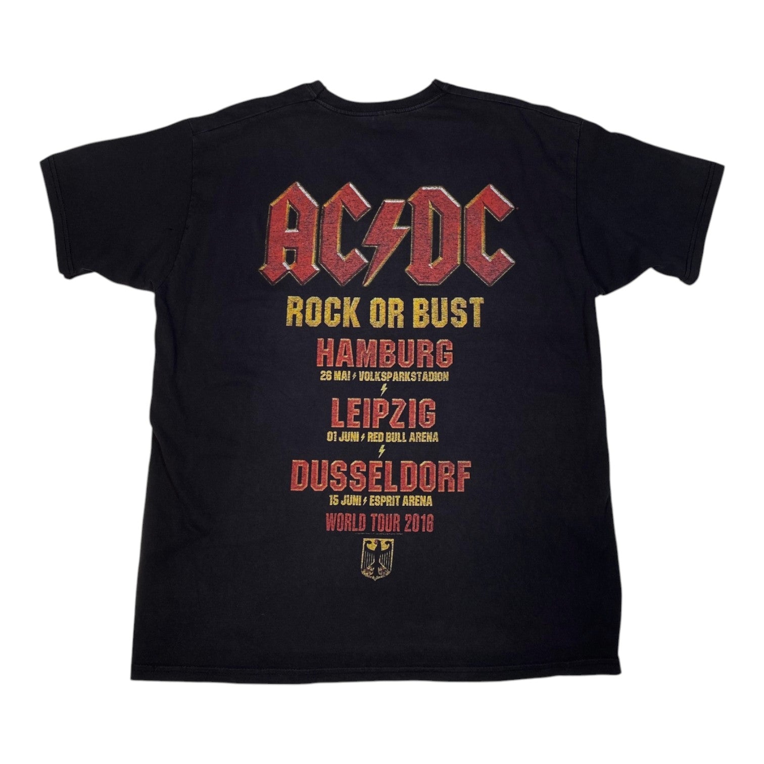 A black short-sleeve t-shirt featuring a large AC/DC 'Rock or Bust' world tour 2016 graphic on the front. The graphic displays the band's name in their signature red and yellow font, followed by the tour cities (Hamburg, Leipzig, Dusseldorf) and dates in red and yellow text, with a small black eagle crest at the bottom.