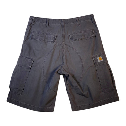 A pair of dark gray Carhartt cargo shorts shown from the back, featuring a central seam, two back welt pockets, and side cargo pockets with the signature Carhartt logo patch.