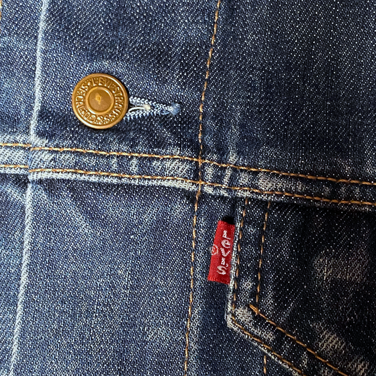 Digg It Thrift & Vintage Levi's denim trucker jacket detail showing brass button and red tab on blue denim fabric