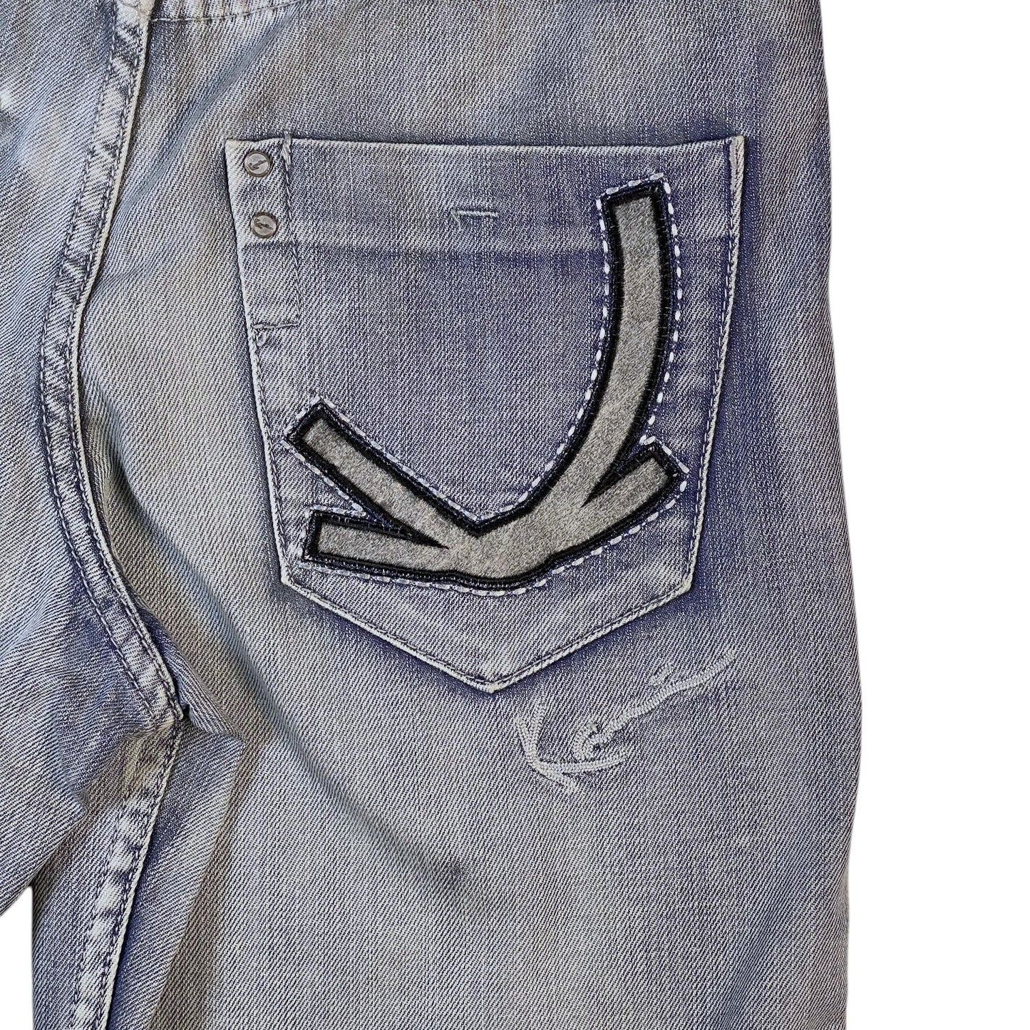 Close-up of a light blue denim jacket showing the back pocket with a distinctive arrow-shaped patch and distressed details.