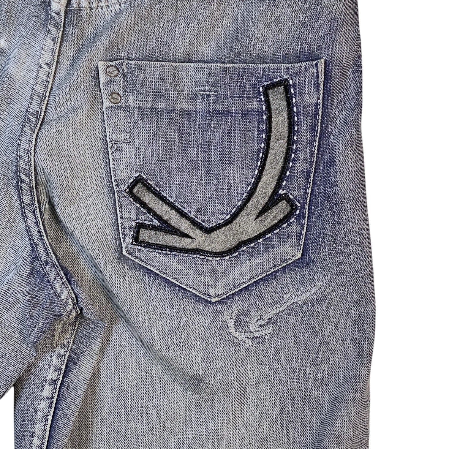 Close-up of a light blue denim jacket showing the back pocket with a distinctive arrow-shaped patch and distressed details.