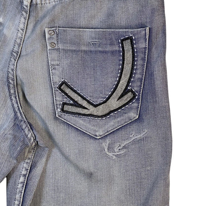Close-up of a light blue denim jacket showing the back pocket with a distinctive arrow-shaped patch and distressed details.