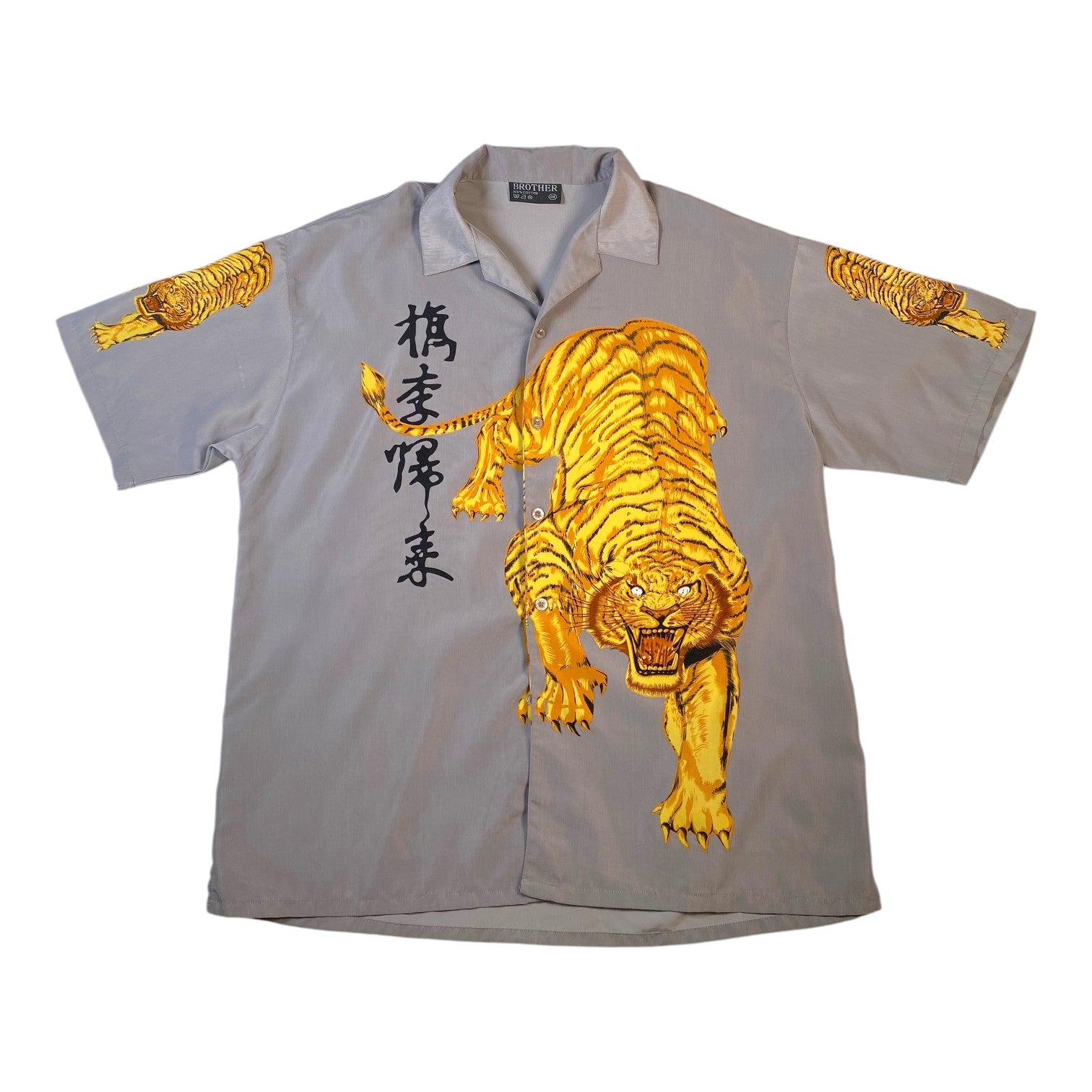 A light gray short-sleeve button-up shirt featuring a large golden tiger graphic on the front, black vertical Japanese characters on the left chest, and smaller tiger prints on both sleeves.