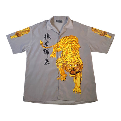 A light gray short-sleeve button-up shirt featuring a large golden tiger graphic on the front, black vertical Japanese characters on the left chest, and smaller tiger prints on both sleeves.