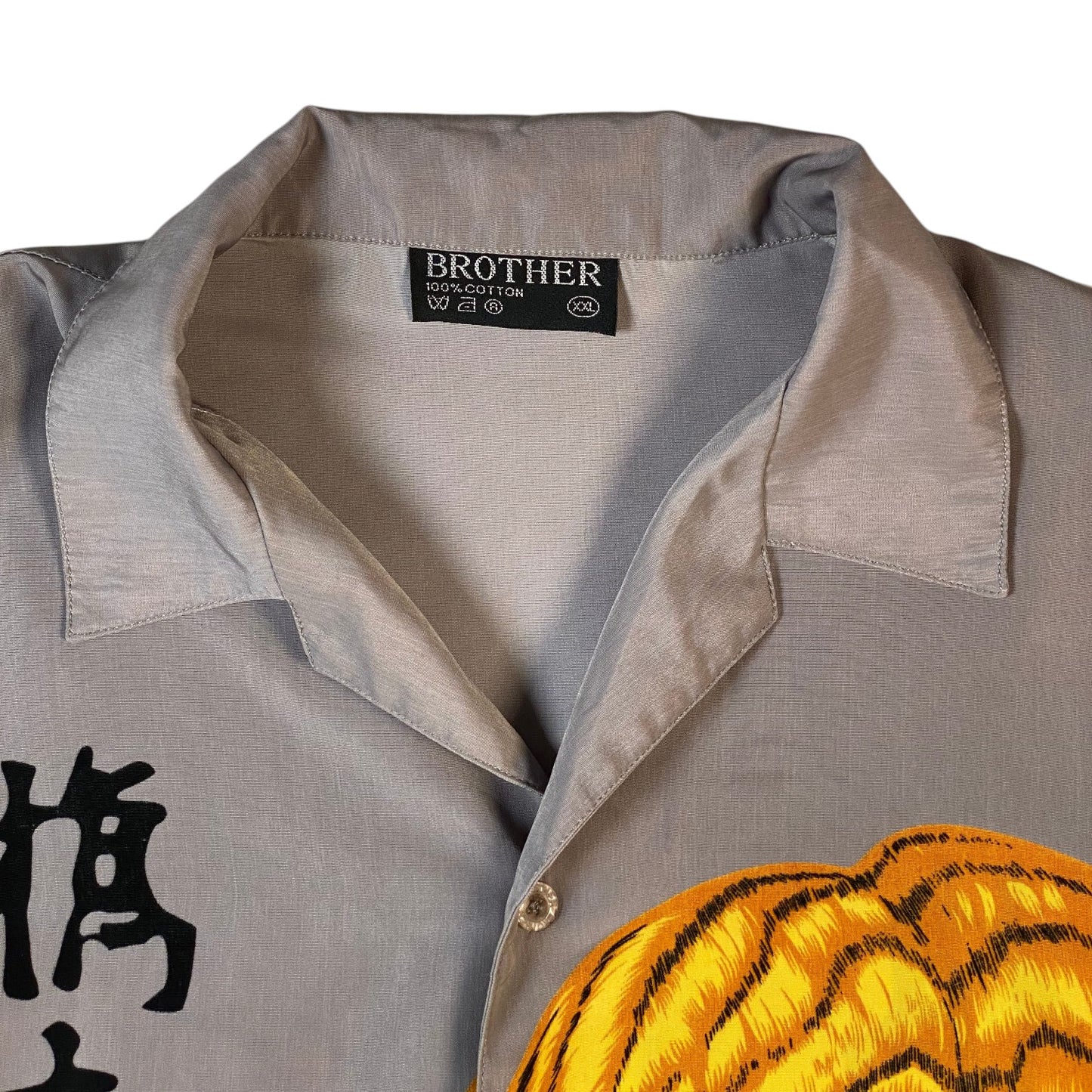 Close-up of a gray short-sleeve button-up shirt with a collar, featuring a black Brother brand label at the inner neck and a yellow and black tiger-stripe graphic across the lower front.