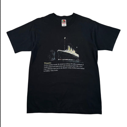 A black short-sleeve crewneck t-shirt featuring a graphic print of the Titanic on the front with a white text description below it, displayed flat against a white background.