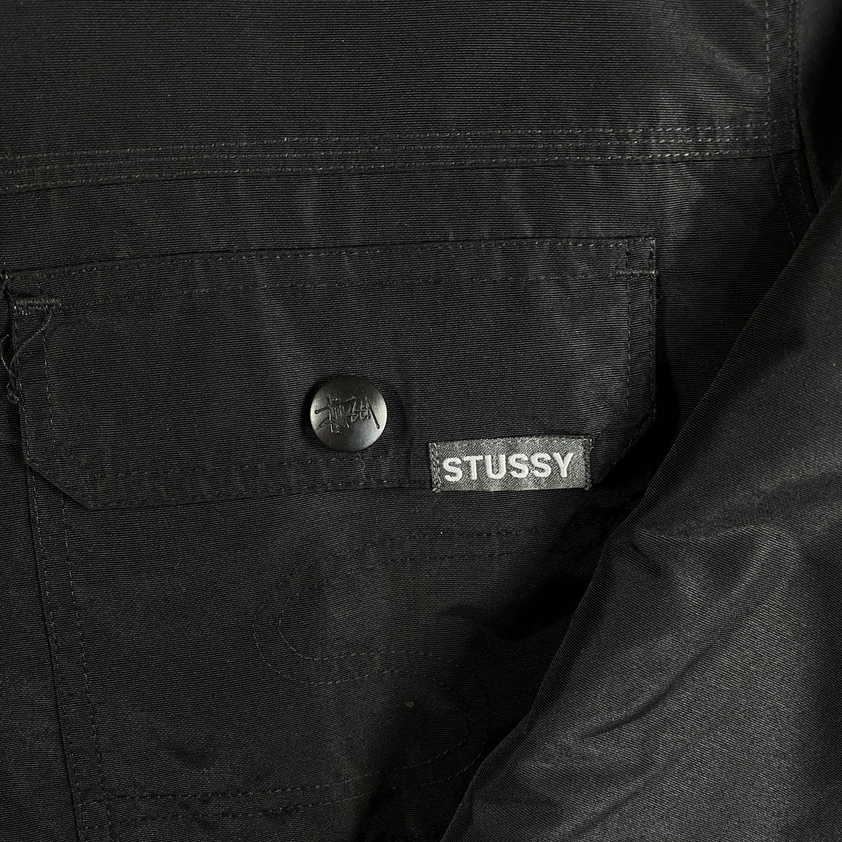 Digg It Thrift & Vintage black Stüssy insulated workwear jacket featuring a snap-front pocket and brand logo tag.