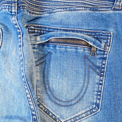 Close-up of the back pocket of light blue denim jeans, showing a zippered pocket with a metal pull tab and contrast stitching.