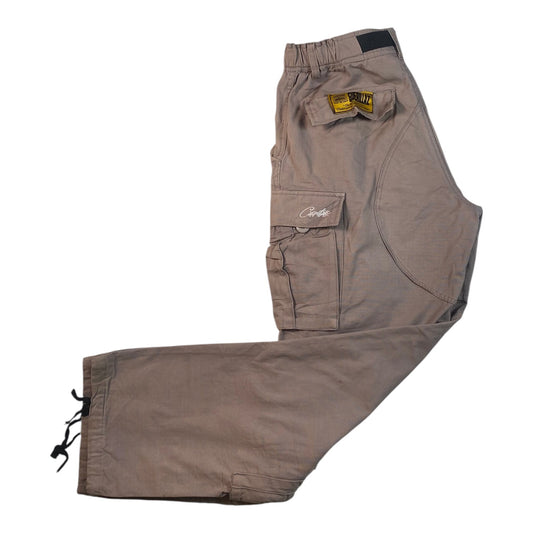 A pair of light brown cargo pants laid flat on a white background, featuring a drawstring ankle cuff, a flap cargo pocket with a white script logo, and a yellow brand patch.