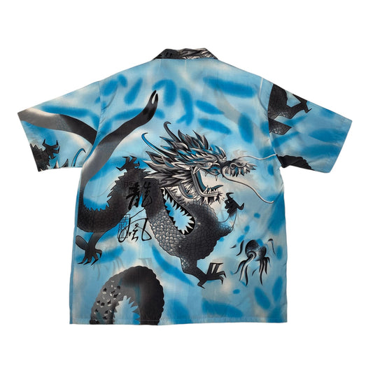 A short-sleeve camp collar shirt featuring a large black and silver dragon design over a blue and white marbled background, displayed flat against a white background.