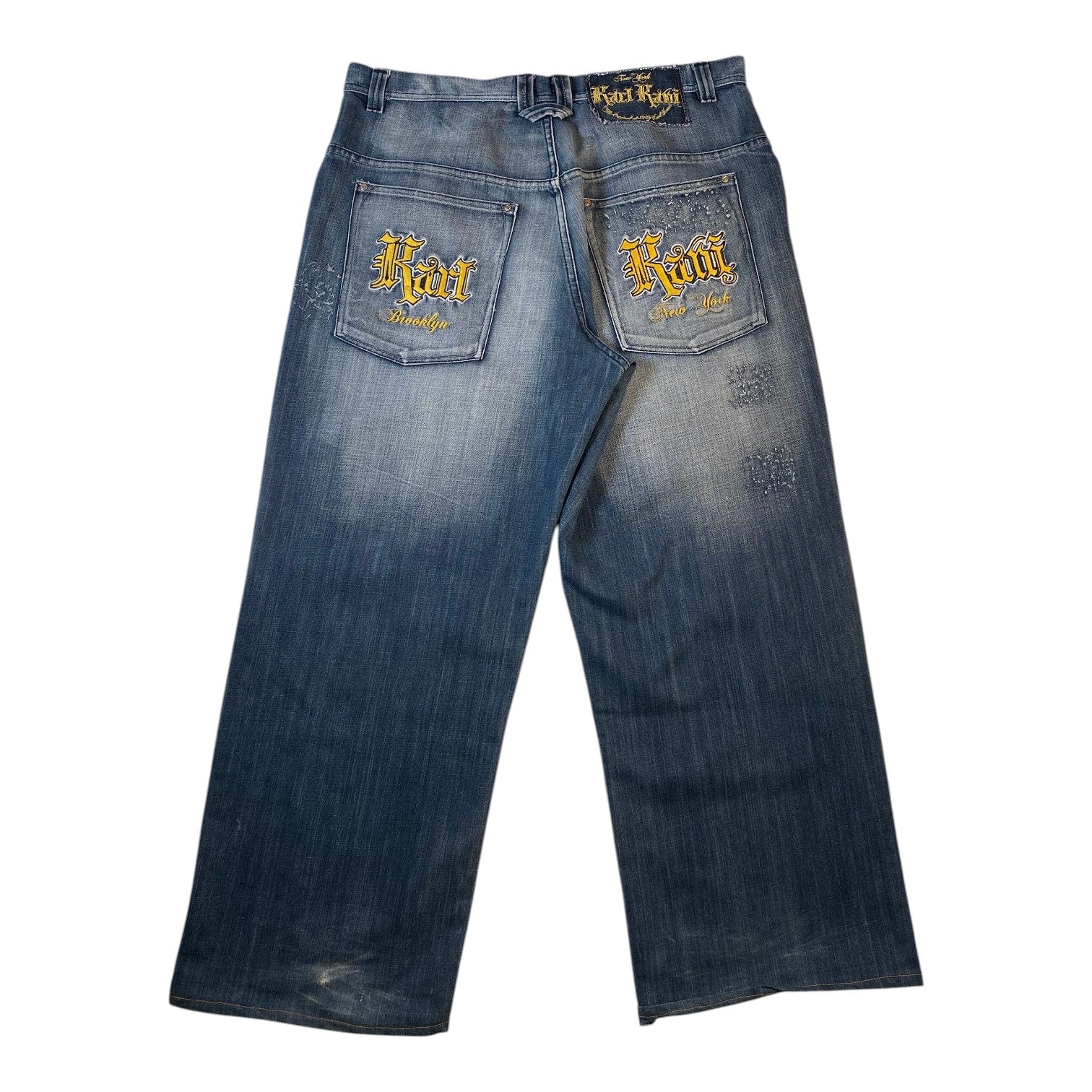 Blue denim jeans with a faded wash, featuring 'Korn' embroidered in gold on both back pockets and a matching 'Korn' label on the waistband, shown against a plain white background.