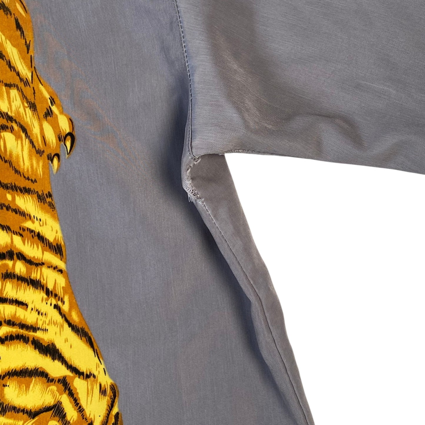 Close-up of a gray garment with a large yellow and black tiger print on the left side, showing fabric texture and a white background.