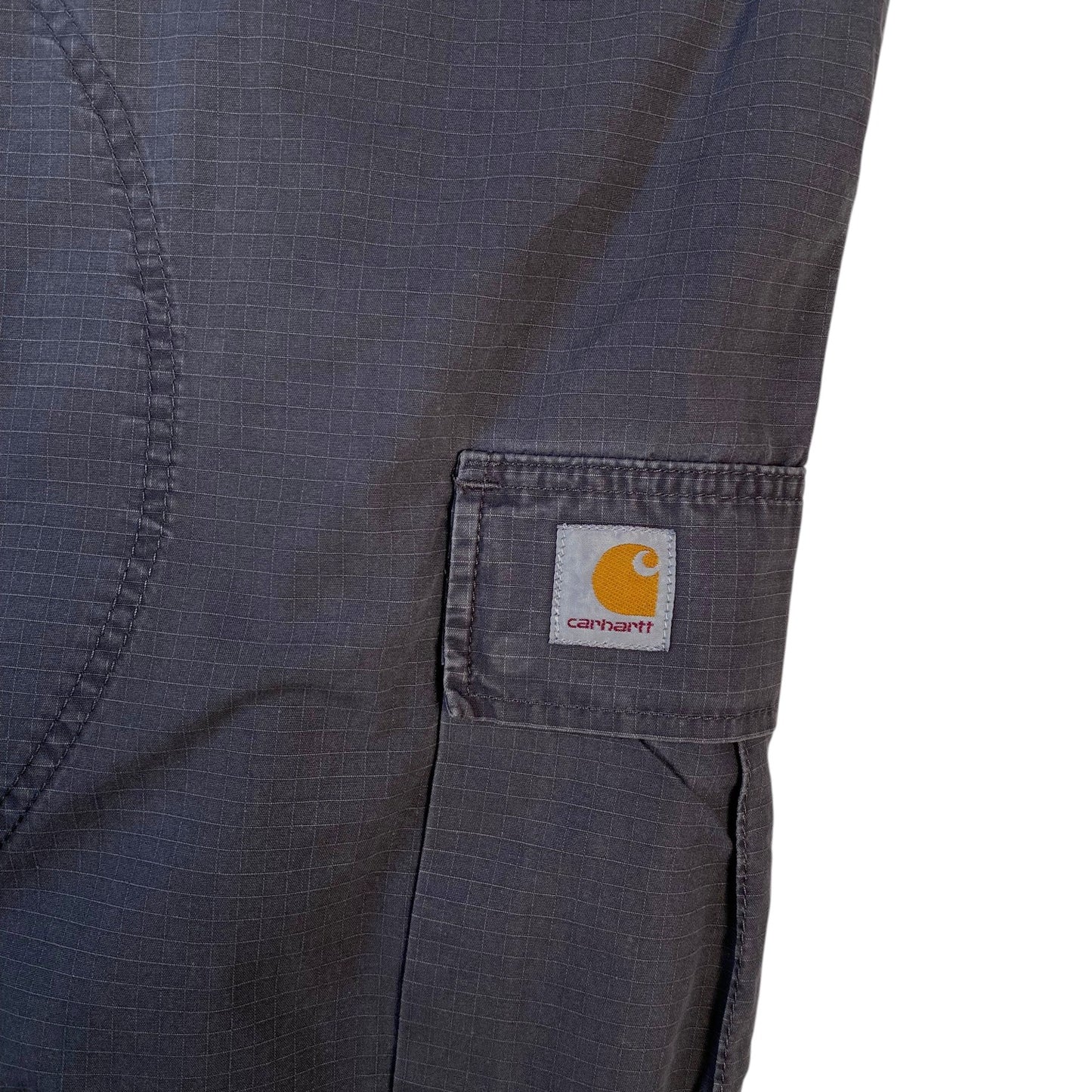 Close-up of dark gray Carhartt fabric with a side pocket showing the brand's signature yellow and white logo patch.