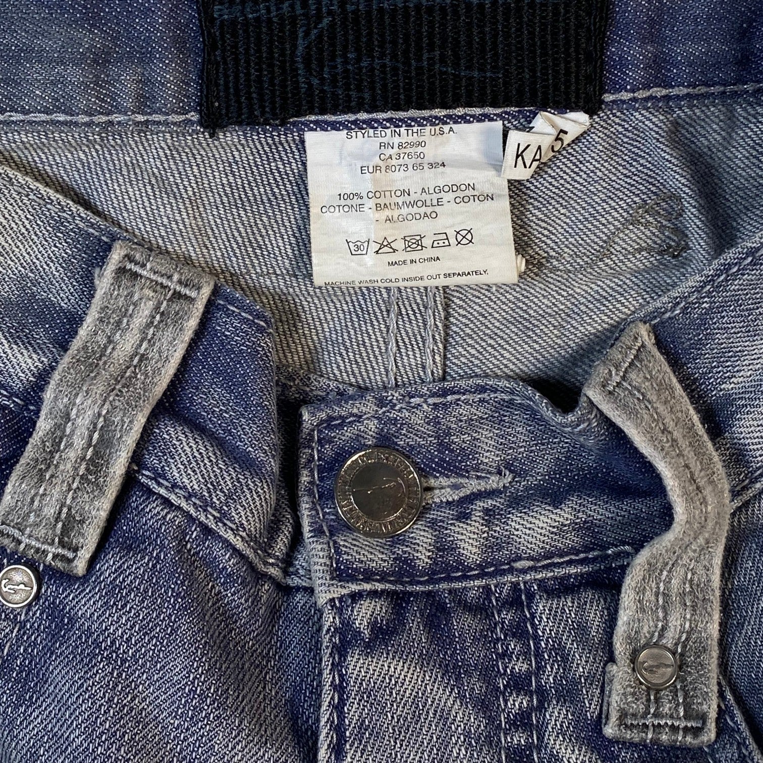 Close-up of blue denim jeans showing the inner waistband, white size and care label, button, and rivets.