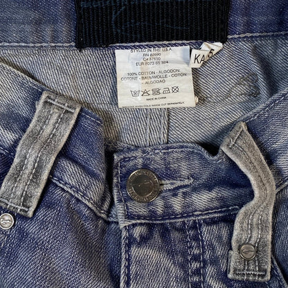 Close-up of blue denim jeans showing the inner waistband, white size and care label, button, and rivets.
