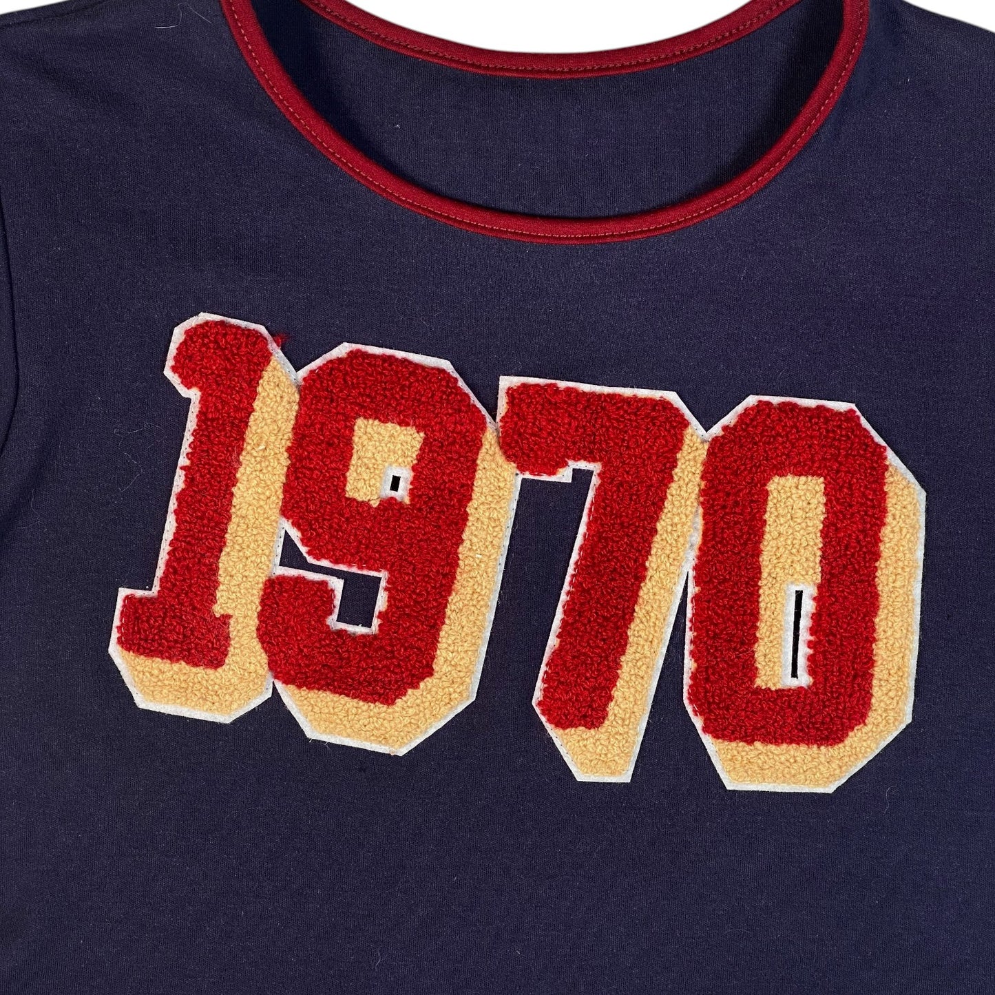 Digg It Thrift & Vintage navy blue top featuring a red and cream 1970 chenille patch graphic and red crew neckline.