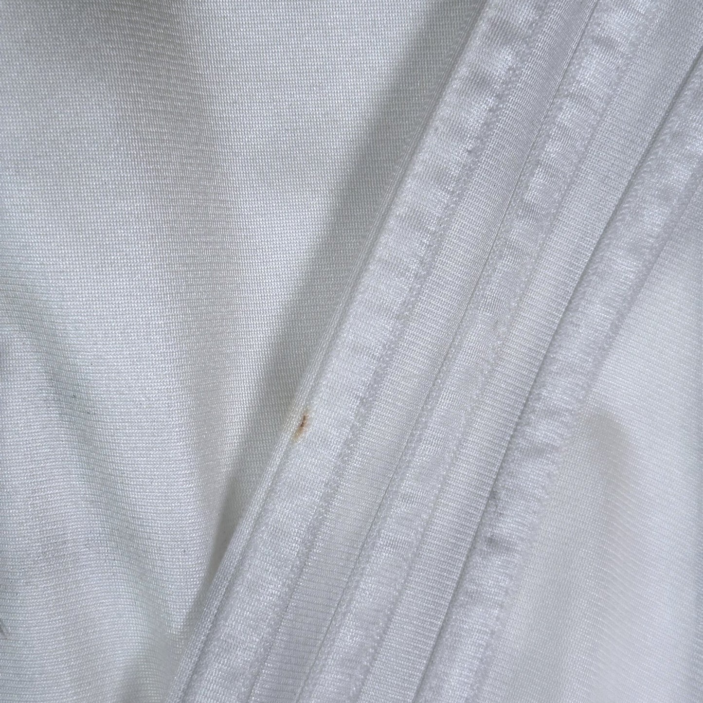 Close-up of white Adidas Chile Rasta track jacket fabric by Digg It Thrift & Vintage showing a small light stain.